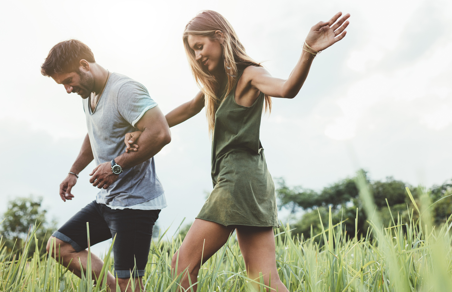 Outdoor shot of young couple walking through meadow hand in hand. Man and woman talking walk through grass field in countryside.